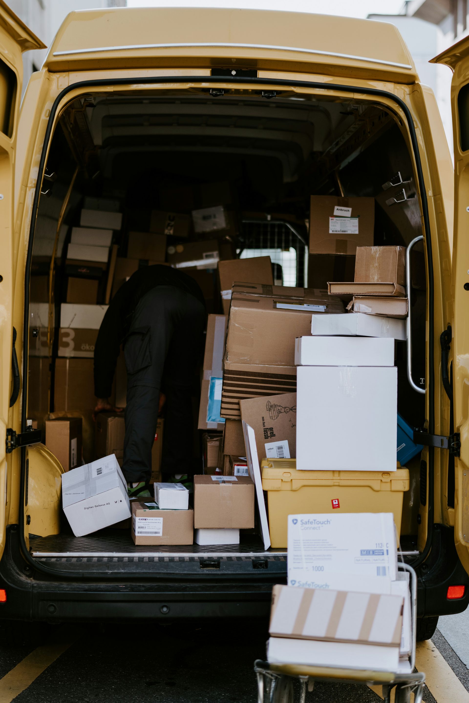 A person in dark clothing loading cardboard boxes into a yellow delivery van